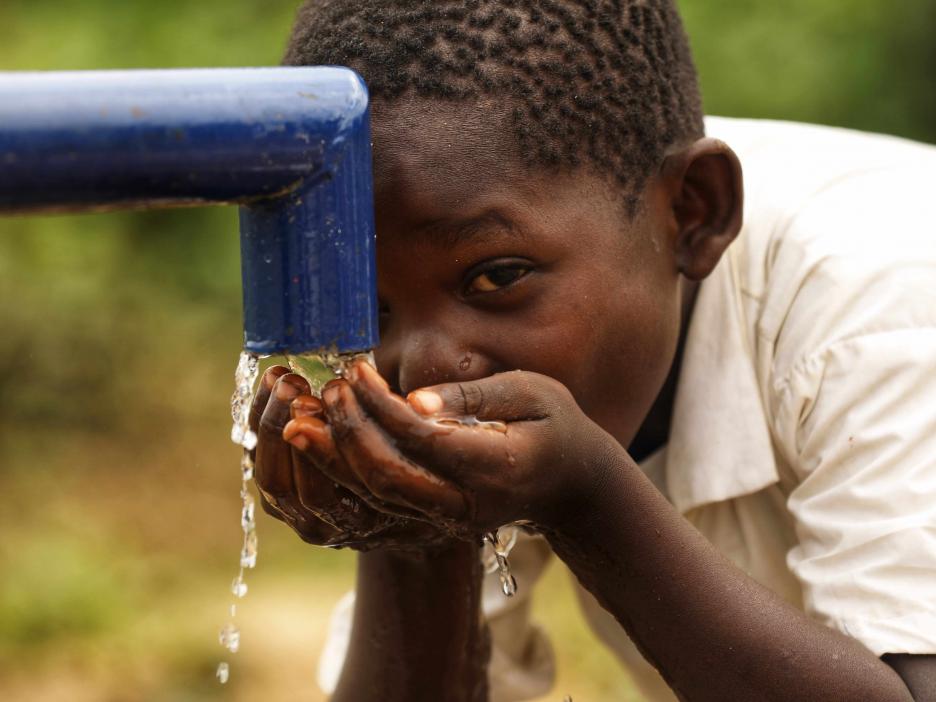Un niño bebe agua potable de una bomba manual recién instalada.